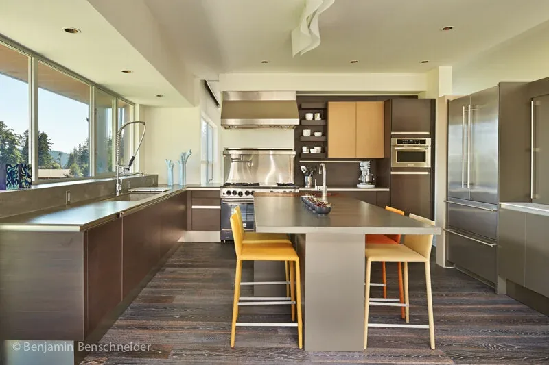 The kitchen features dark cabinetry with an island and stainless steel appliances under a wide window bringing in natural light.