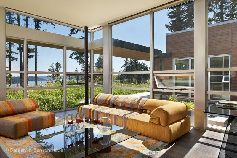 Living room of Island Sanctuary with floor-to-ceiling corner windows providing natural views and striped couches.