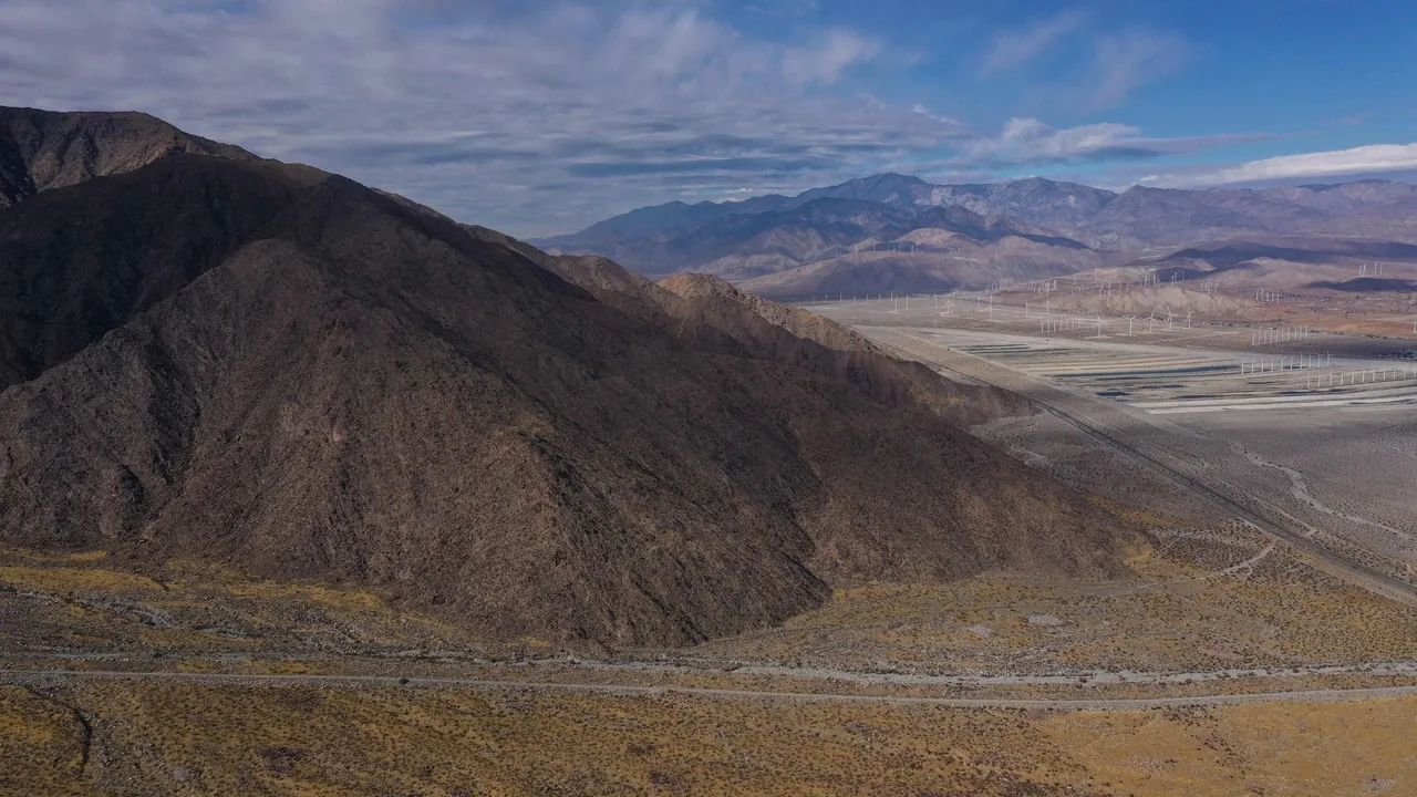 Desert mountain landscape with rocky slopes and desert vegetation under scattered clouds.