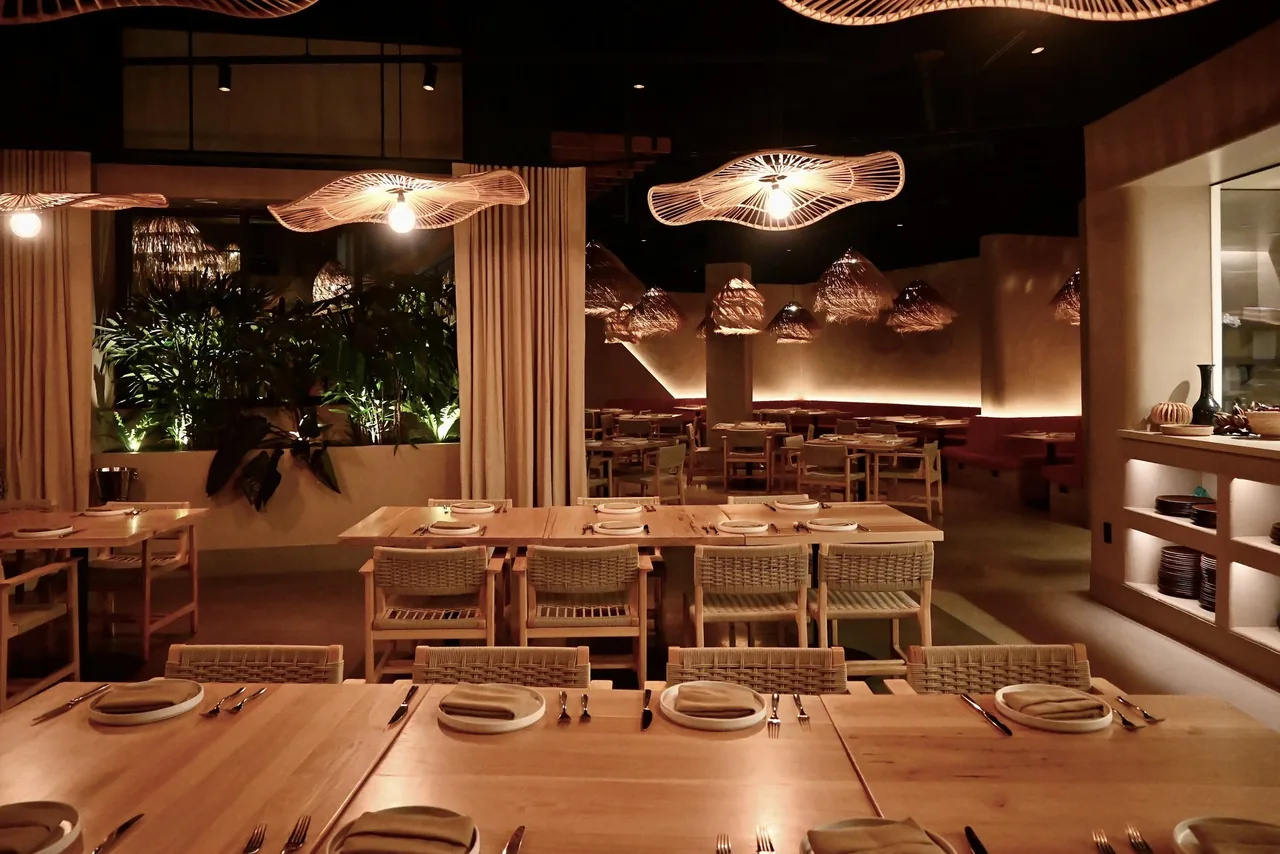 Wood-furnished restaurant interior with sculptural pendant lighting and woven chairs.