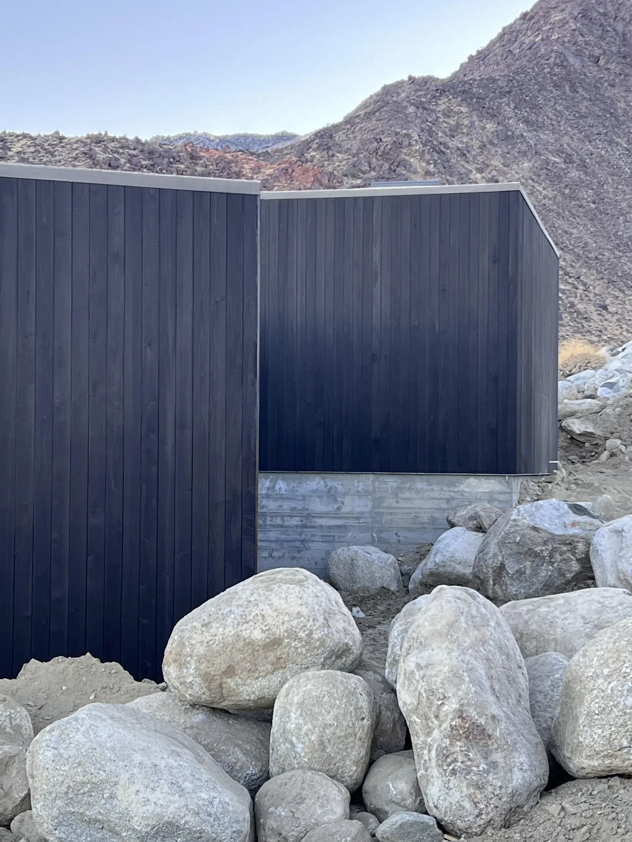 Close-up view of dark wood siding on an elevated cabin against a rocky hillside.