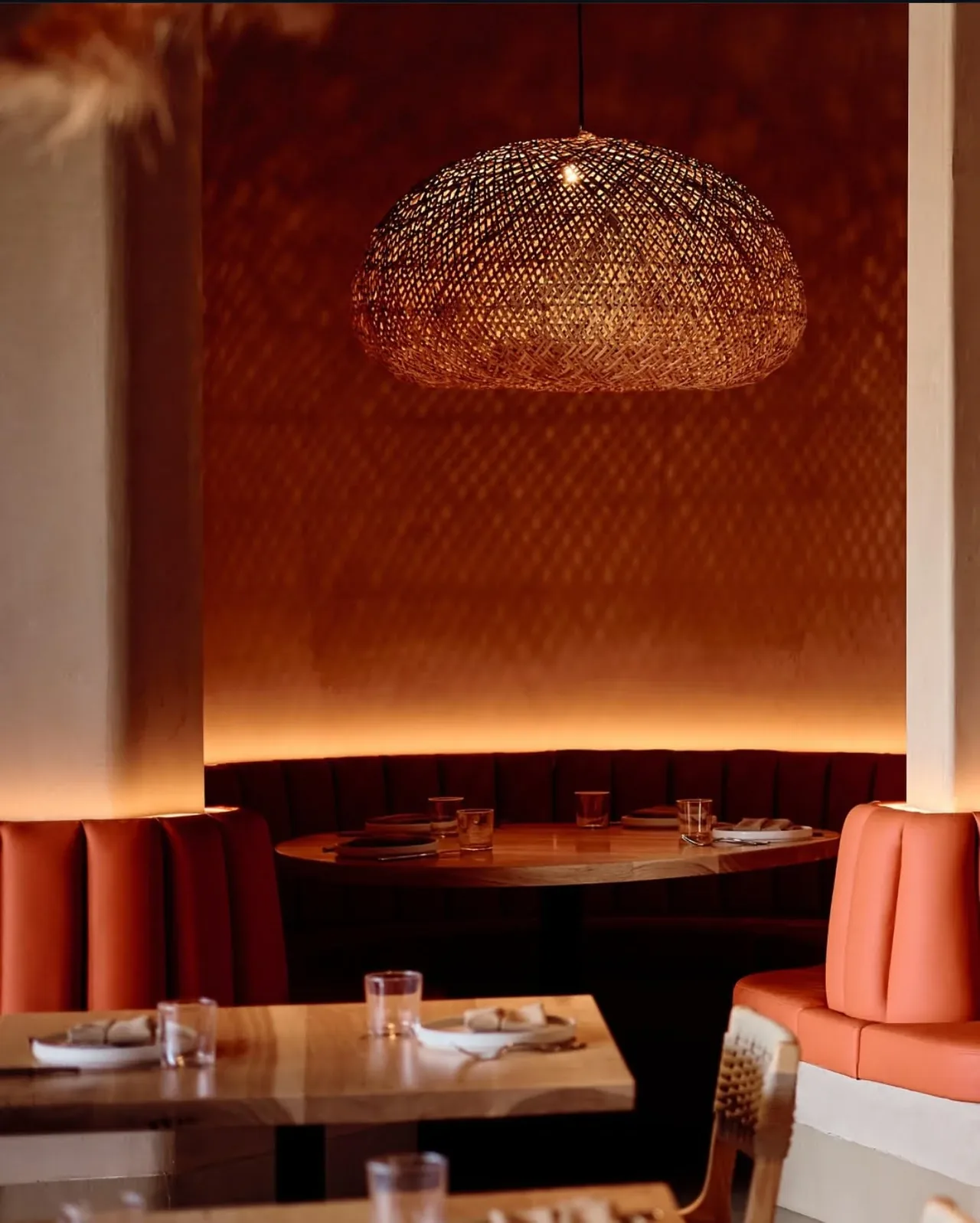 Cozy dining area with curved booth seating and a woven pendant light creating textured shadows.