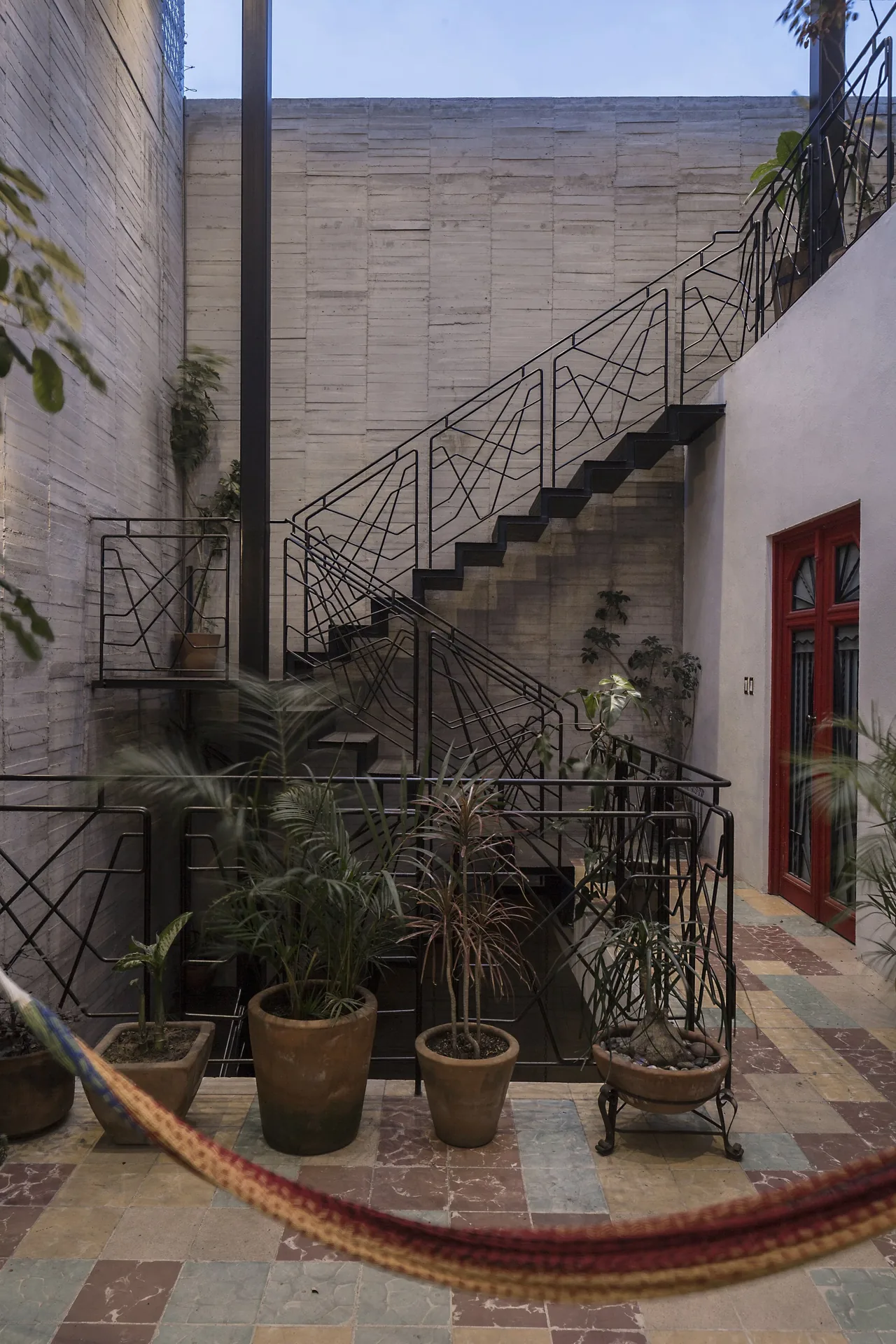 Interior courtyard featuring black metal stairs with geometric railings, concrete walls, and potted plants on a colorful tile floor.