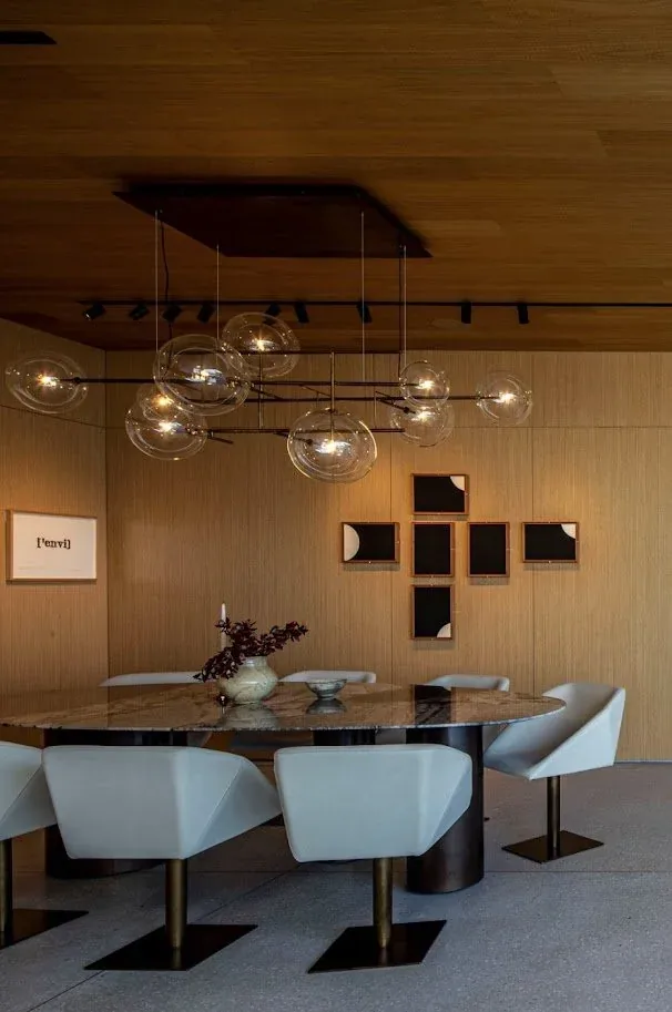 Dining space featuring an oval marble table, white swivel chairs, and a multi-globe pendant light over it.