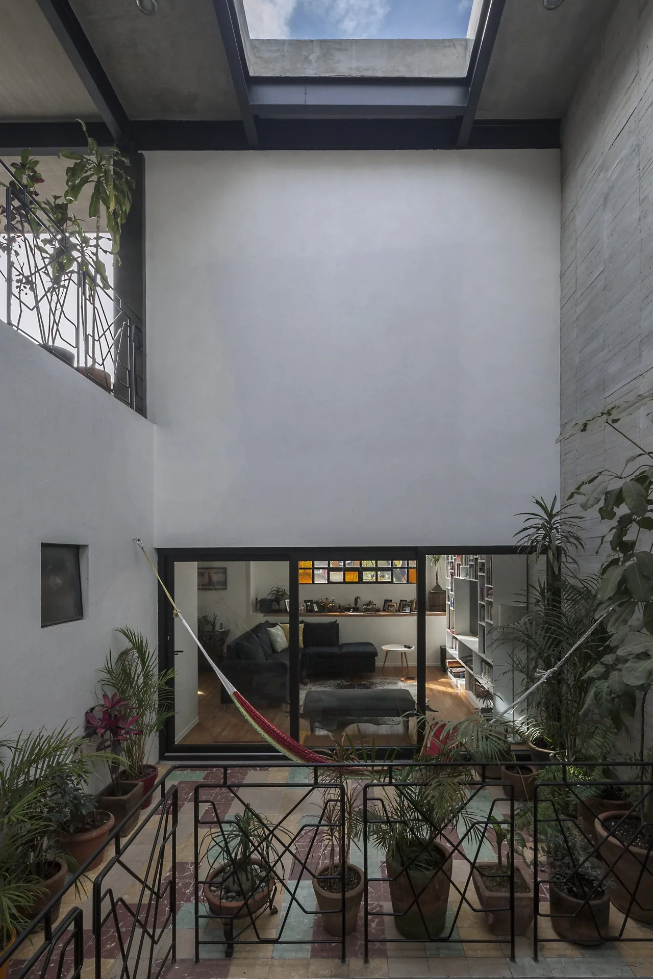 A small interior courtyard features a hammock, various potted plants, and a large skylight, with a view into a living room through glass doors.