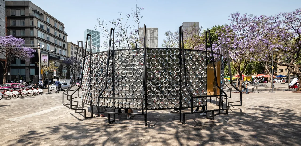 Circular outdoor installation with a black metal frame and reflective circular discs in an urban setting.