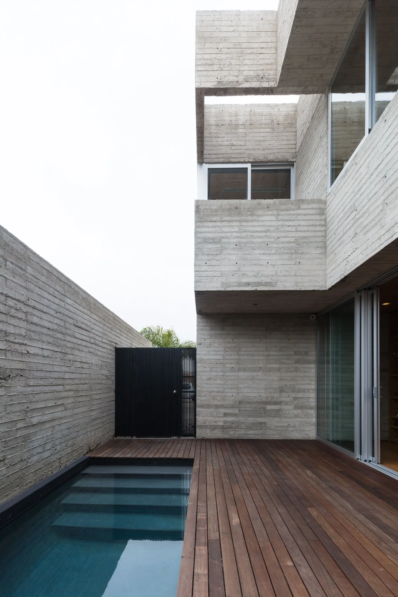 A modern exterior area featuring board-formed concrete walls and a wooden deck alongside a small pool.
