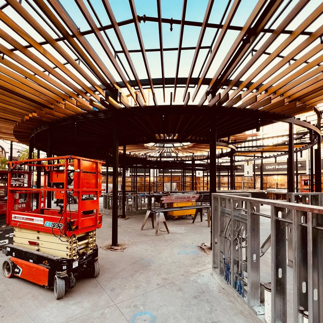 Outdoor construction with circular black metal framework and horizontal wood slats forming a pergola-like roof.