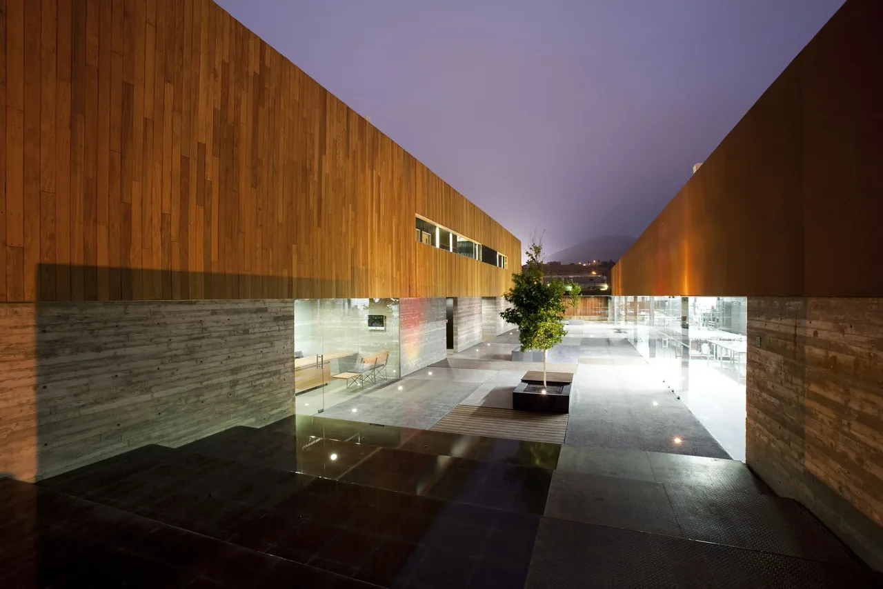 Modern courtyard featuring vertical wood siding over board-formed concrete walls, glass partitions, and recessed lighting.