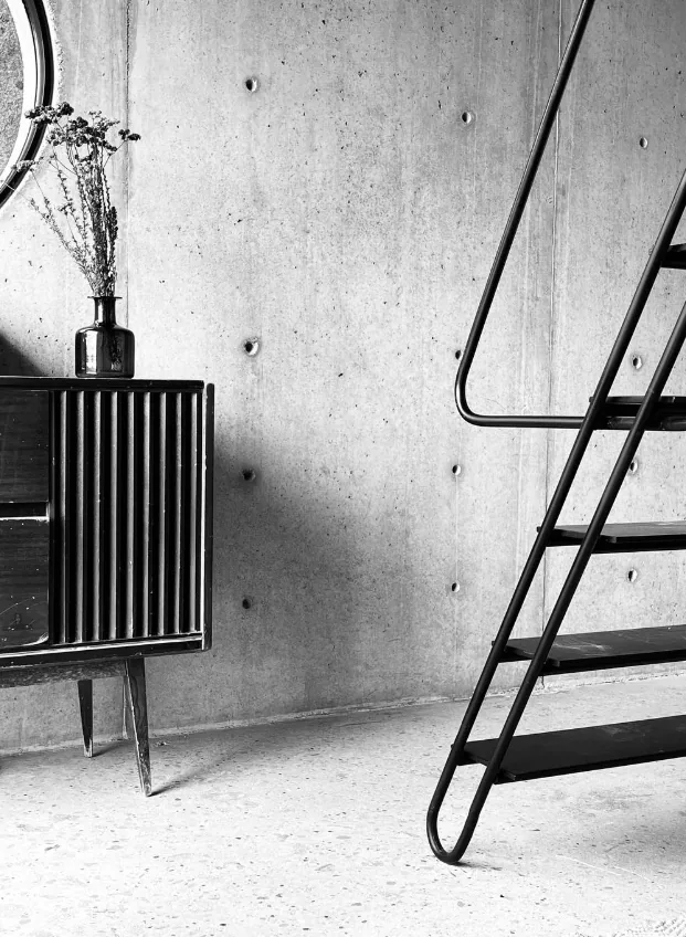 Interior view featuring a black metal open stair and slatted wooden cabinet against a raw concrete wall.