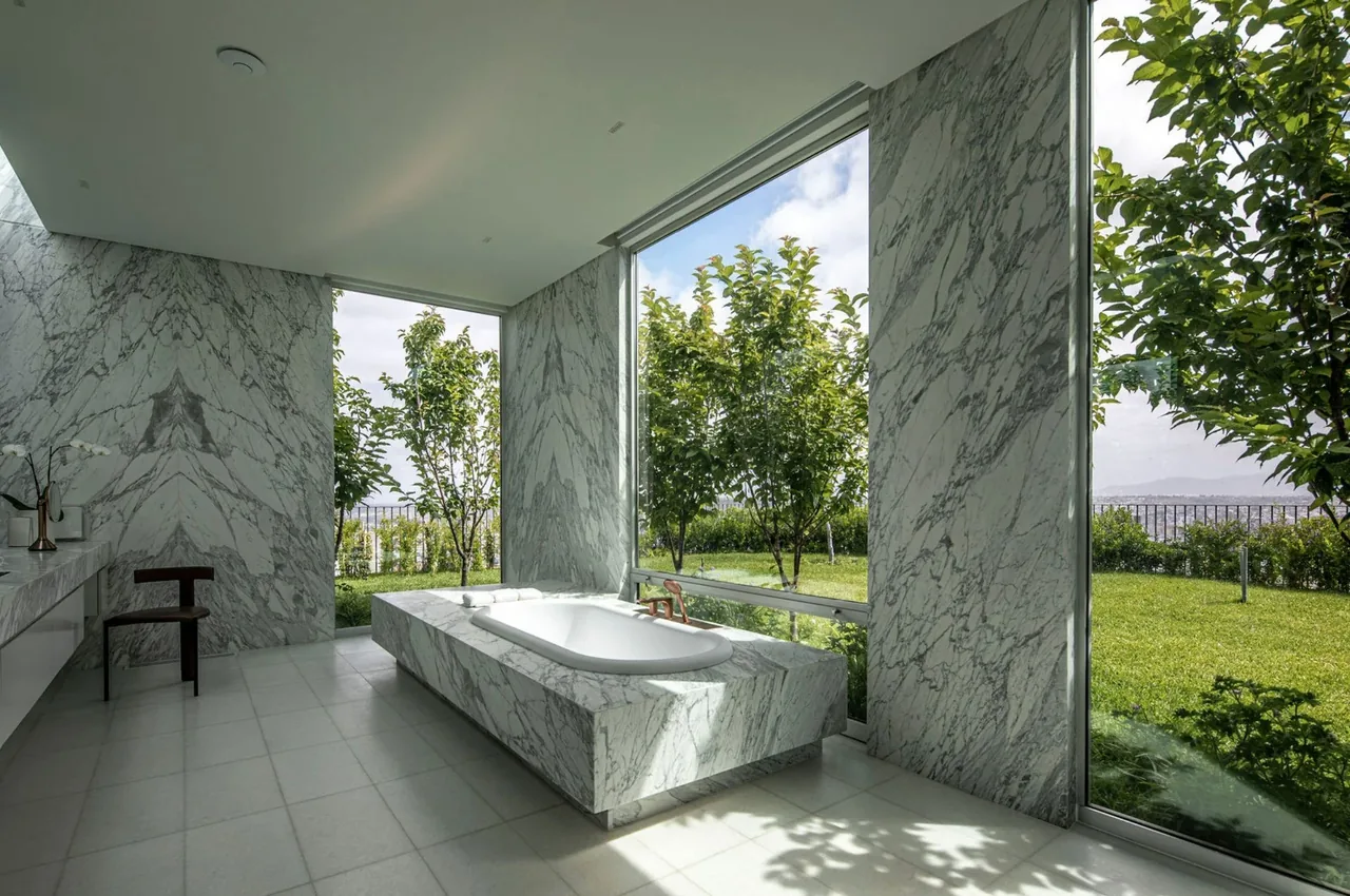 Bathroom featuring a marble bathtub surrounded by floor-to-ceiling windows with garden views.