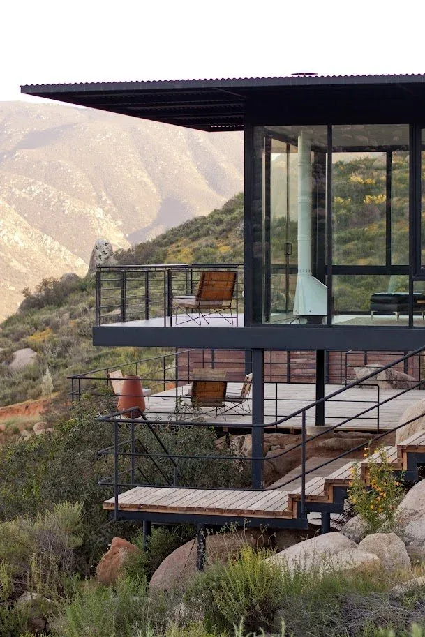 Modern outdoor multi-level deck with seating and black metal railings overlooking natural terrain.