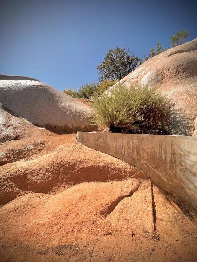 Concrete retaining wall near natural rocky formations and sparse vegetation.