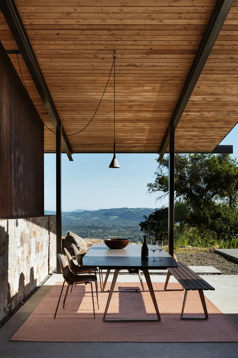 Covered outdoor dining space with wooden ceiling slats and a view of distant hills.