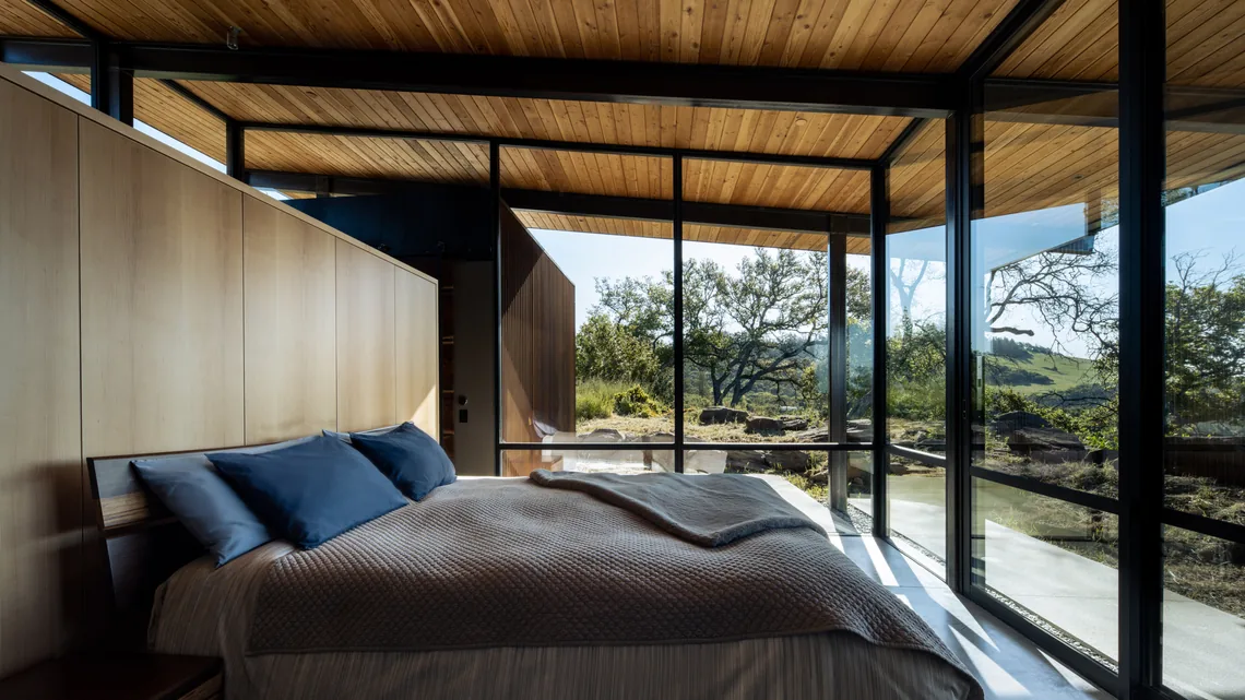 Bedroom in HOUSE FOR A NEW BEGINNING featuring floor-to-ceiling glazing and wood ceiling slats with a scenic natural view.
