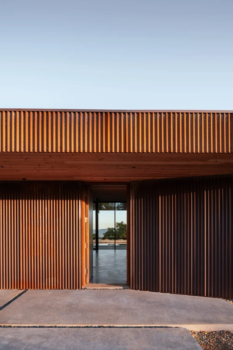 House entry featuring rusted steel siding and a wood ceiling with a visible interior glimpse through the doorway.