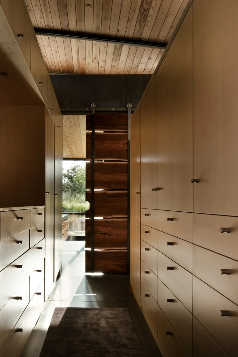 Storage-lined hallway with wood panel ceiling and a sliding wooden door, leading to an outdoor view.