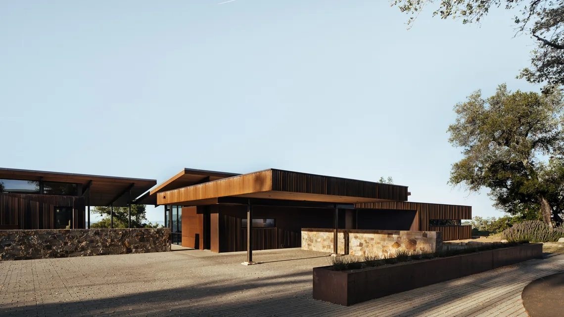 House for a New Beginning features dark wood cladding, stone retaining walls, and a paving stone driveway in a modern style.