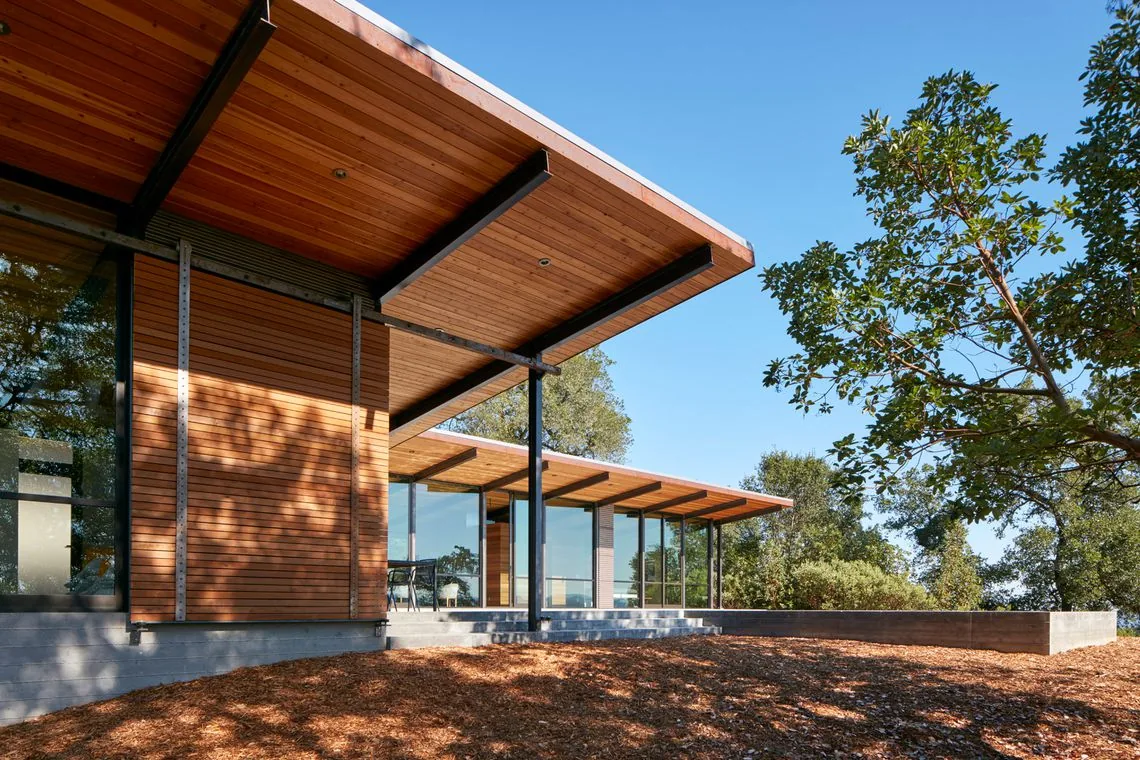 Split Rock Springs Ranch shows modern design with wood cladding and large windows under overhanging eaves.