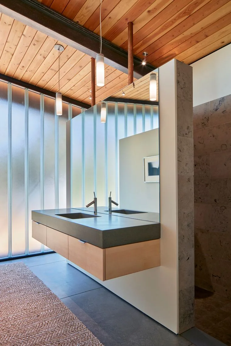 Double floating vanity with dark countertop beneath a wooden ceiling in a bathroom with frosted glass walls.