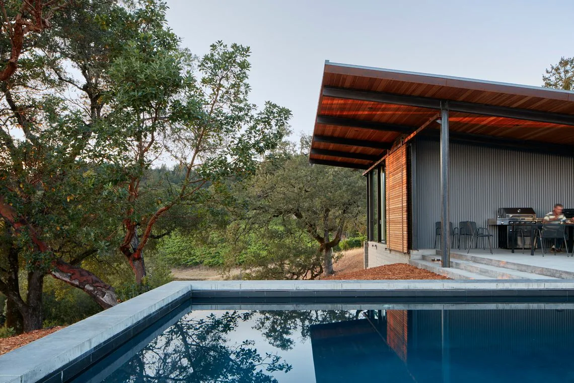 Split Rock Springs Ranch by Nielsen Schuh Architects features a corrugated metal exterior next to a pool and woodland landscape.