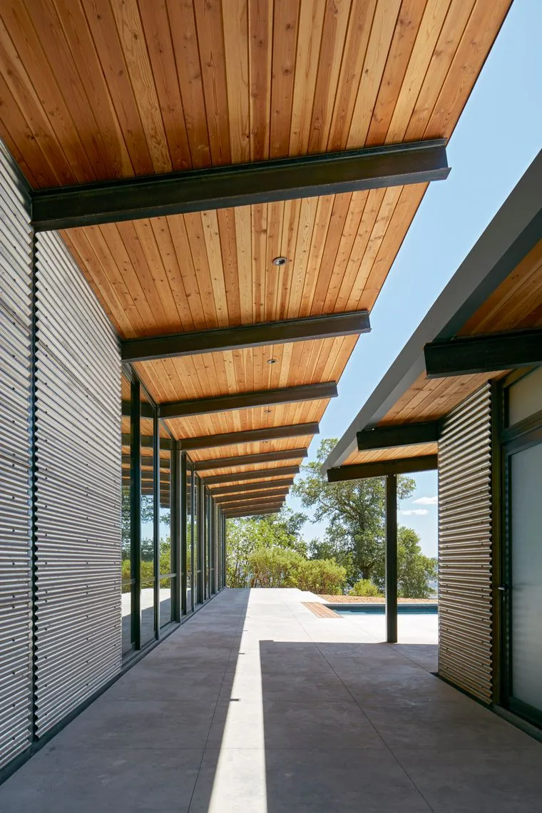 Covered patio with wood soffit ceiling and corrugated metal siding, overlooking a pool and natural landscape.