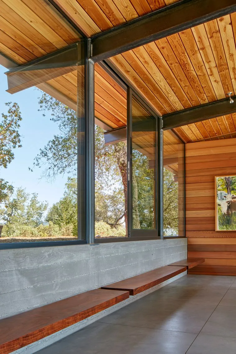Room corner featuring wooden ceiling and walls, large black-framed glass windows, and concrete lower walls with built-in wood benches.