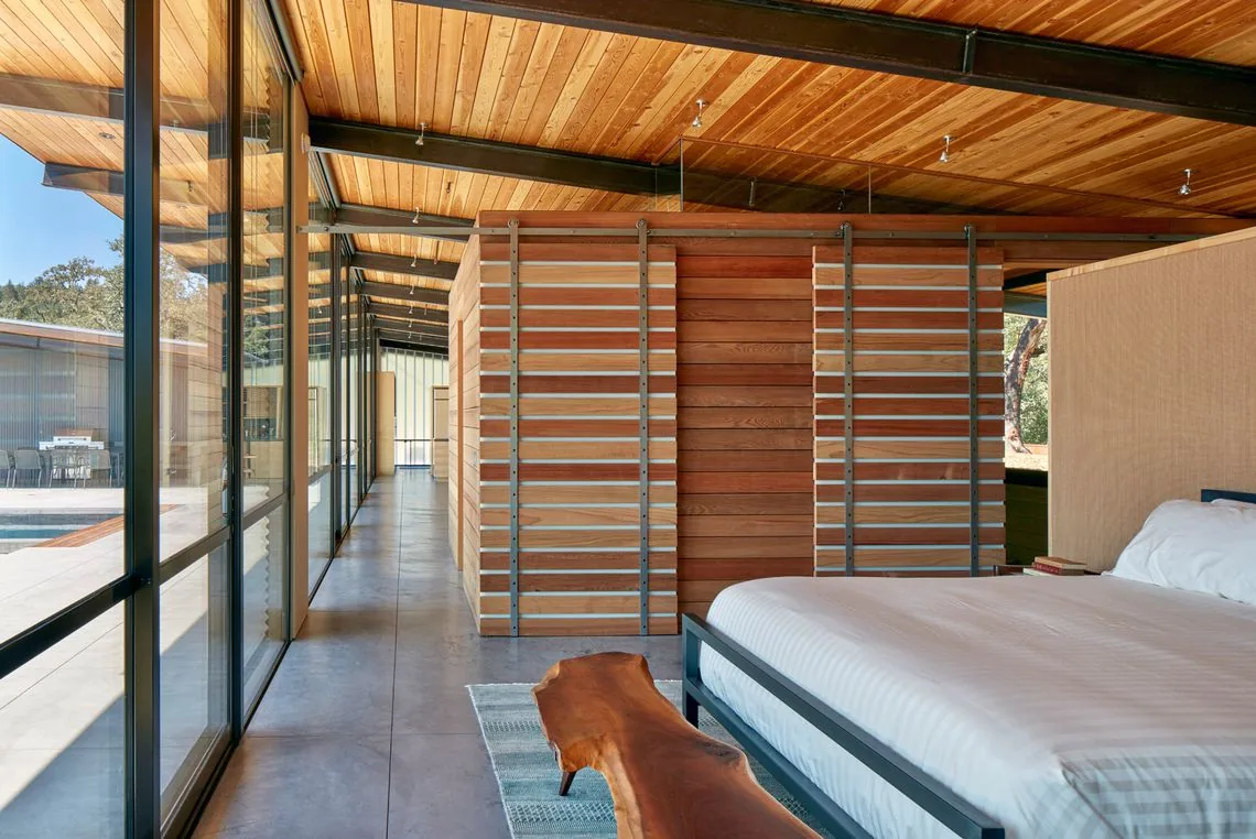 Bedroom features a wood-paneled ceiling, concrete floor, and floor-to-ceiling glazing with black frames.