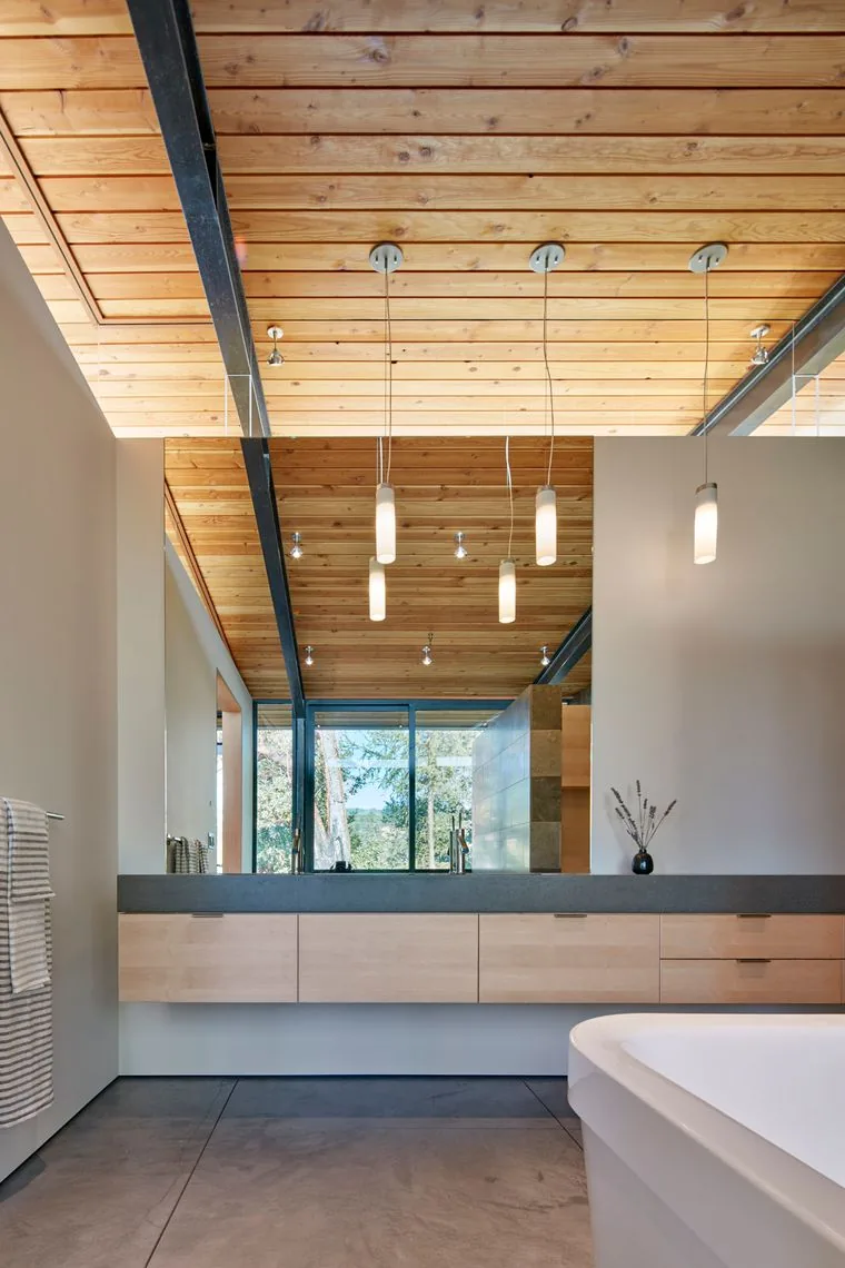 Modern bathroom features wood-paneled ceiling, floating vanity with light wood drawers, concrete floors, and cylindrical pendant lighting.