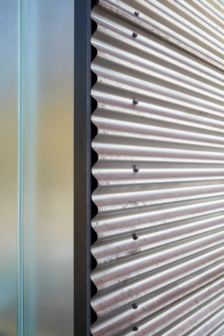 Detail of corrugated metal siding with adjacent frosted glass and black framing at Split Rock Springs Ranch.
