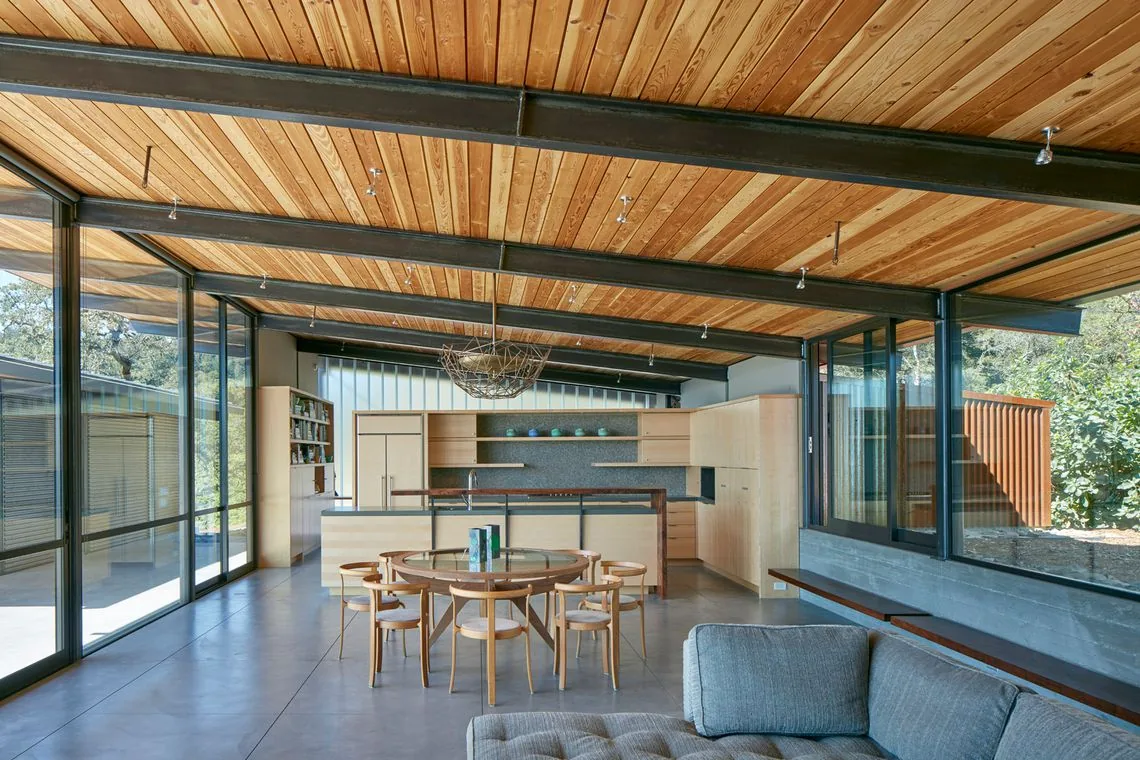 Living and kitchen space featuring wood paneled ceiling, large glass windows, and concrete flooring at Split Rock Springs Ranch.