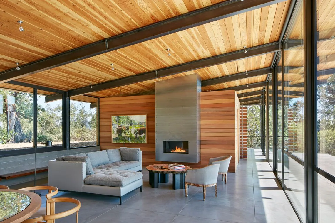 Living room in Split Rock Springs Ranch by Nielsen Schuh Architects features wood soffit ceiling, metal fireplace surround, and floor-to-ceiling glazing.