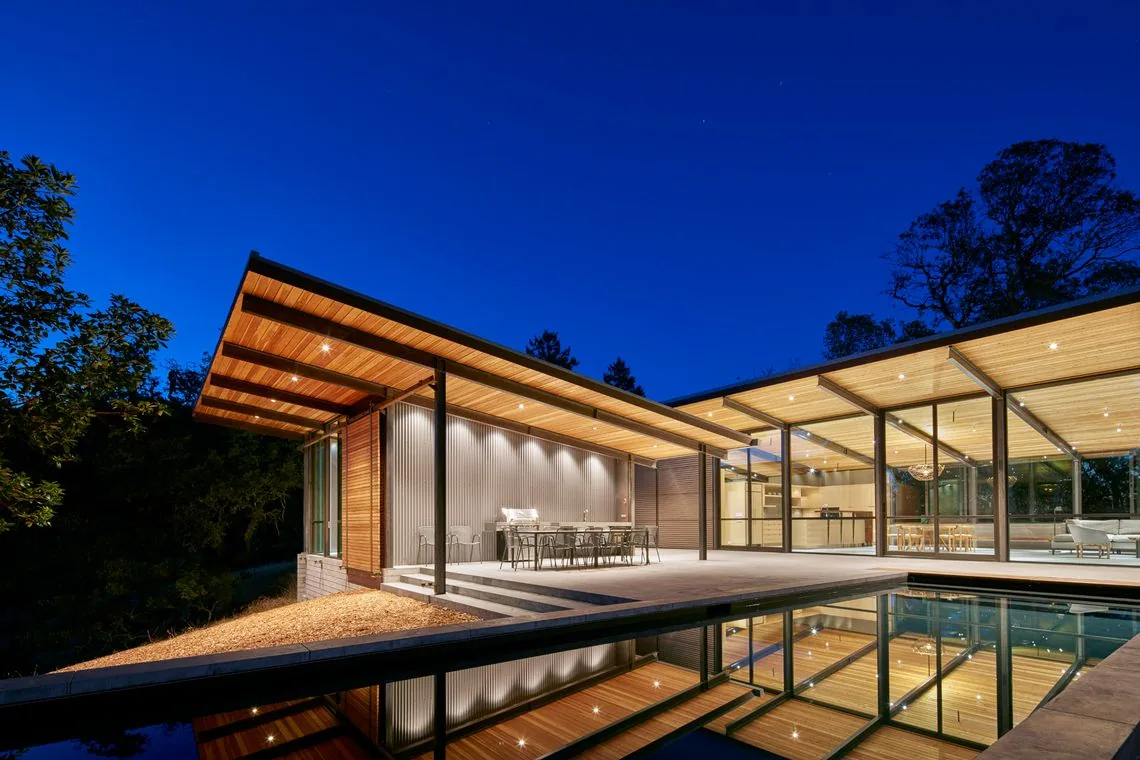 Modern house at night with overhanging wood eaves and reflecting pool at Split Rock Springs Ranch.