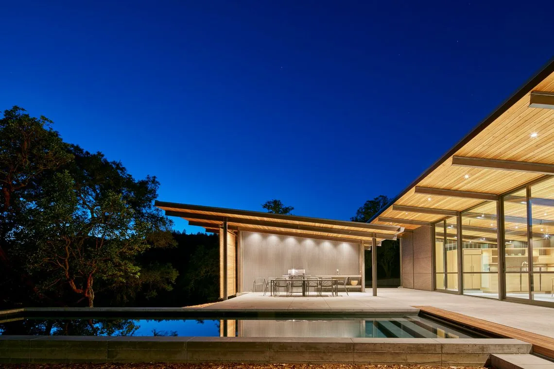 Split Rock Springs Ranch features a modern home with extensive overhanging eaves, a sloping wood ceiling, and outdoor dining by a reflecting pool.