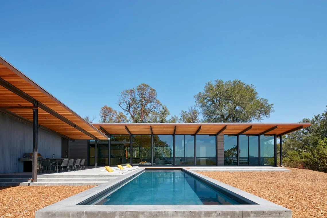 Modern house features a flat roof with wood soffit and floor-to-ceiling glass walls opening onto the pool area at Split Rock Springs Ranch.