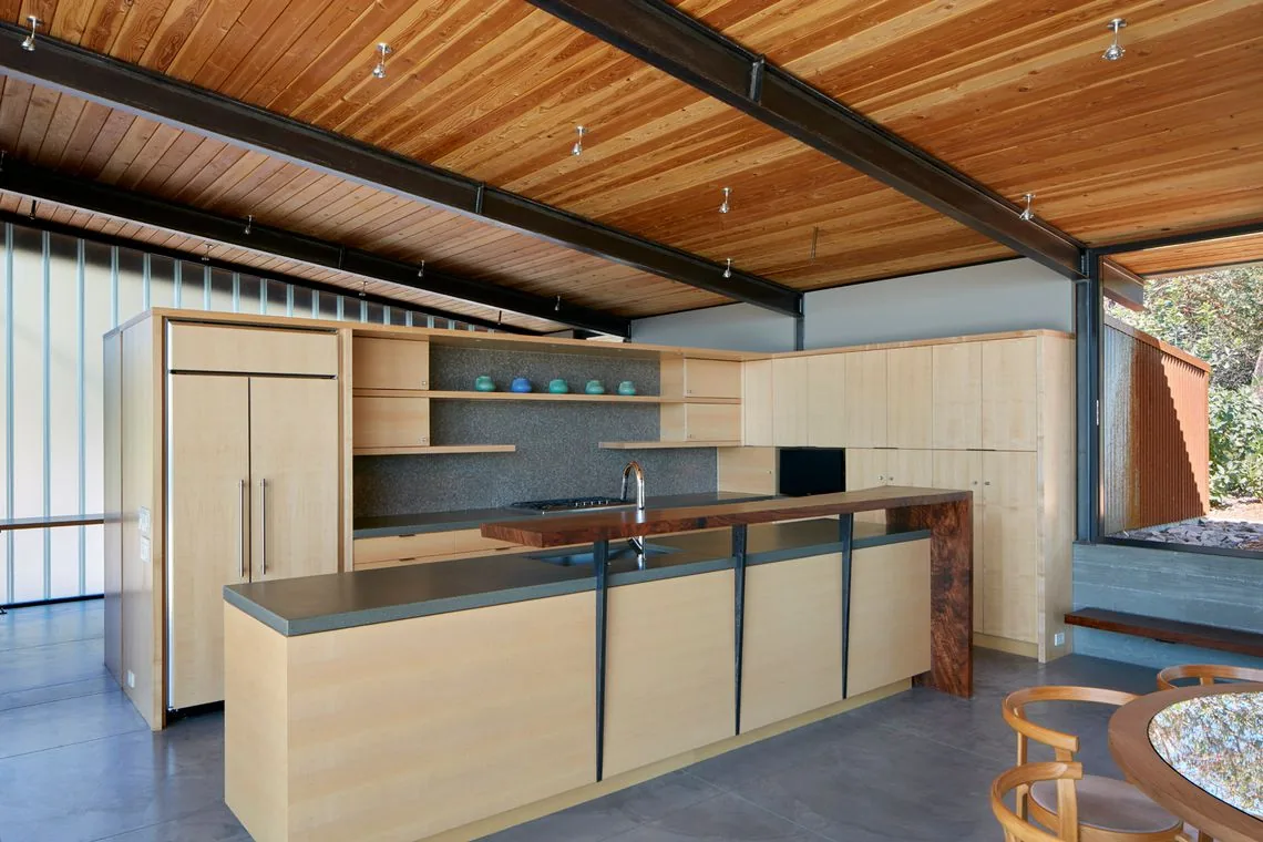 Kitchen interior of Split Rock Springs Ranch featuring light wood cabinetry and a concrete floor with exposed steel beams.