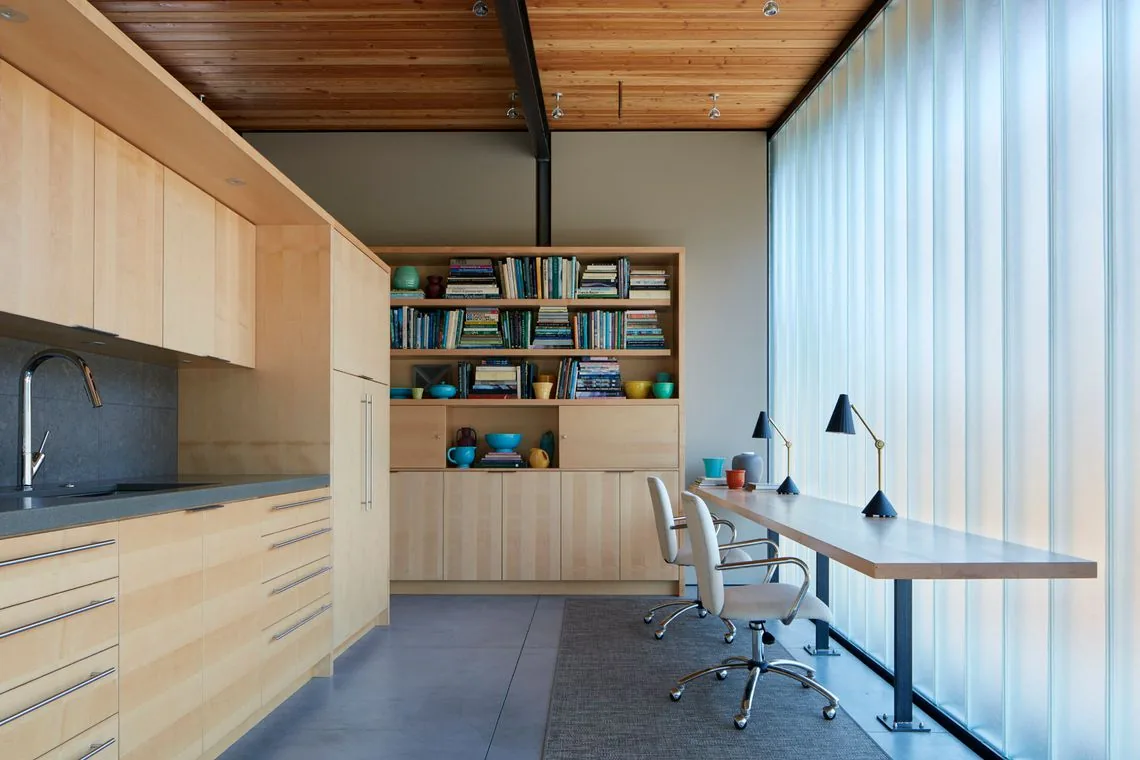 Home office with wood cabinetry, built-in shelves, and frosted floor-to-ceiling windows providing soft natural light.