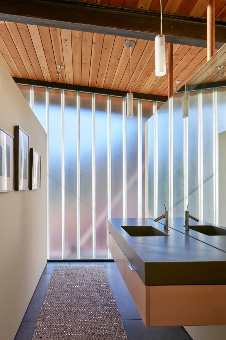 The Split Rock Springs Ranch bathroom features a floating vanity with integrated sinks and frosted glass walls beneath a wood plank sloping ceiling.