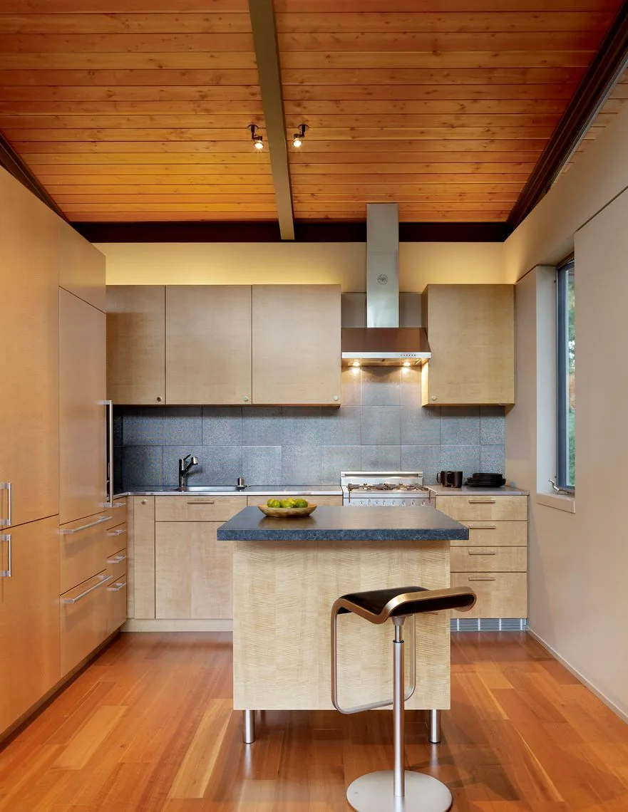 The Sonoma Mountain House kitchen features wood-paneled cabinets, a wood plank ceiling, and a dark countertop island with a metal stool.