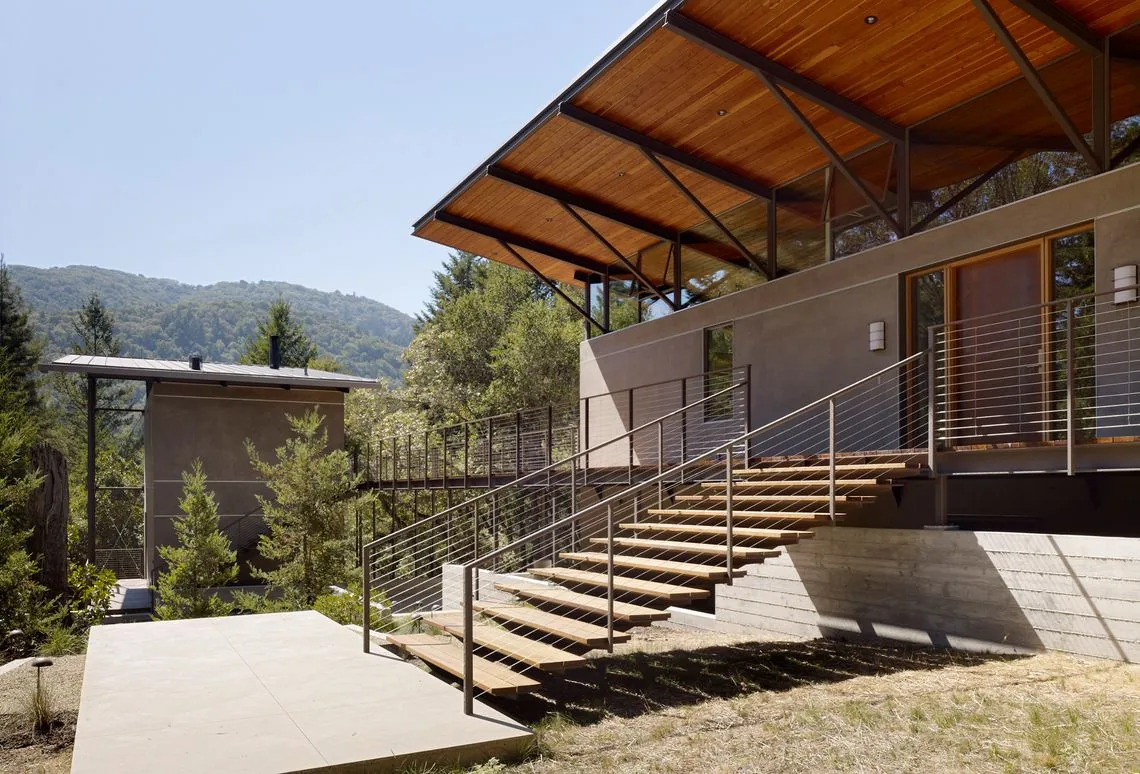 Modern Sonoma Mountain House features a raised concrete foundation, wood-paneled overhanging roof, and metal railings on floating exterior stairs.
