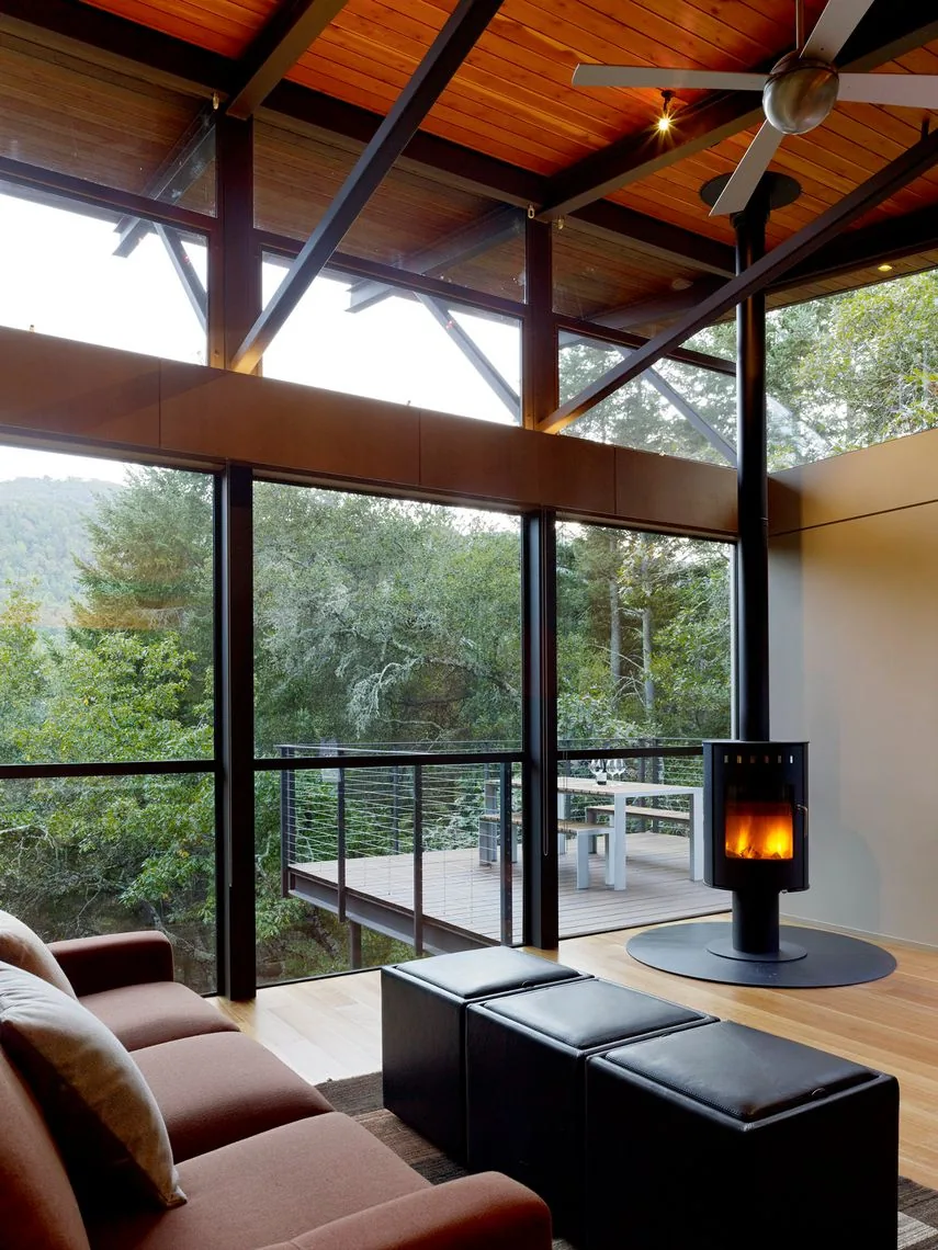Living room features a suspended wood stove, large windows, and a ceiling fan with outdoor deck access.