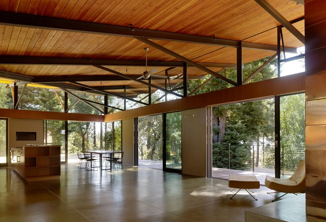 Sonoma Mountain House features an open-plan living and dining space with floor-to-ceiling windows and a wood-paneled ceiling with steel support beams.