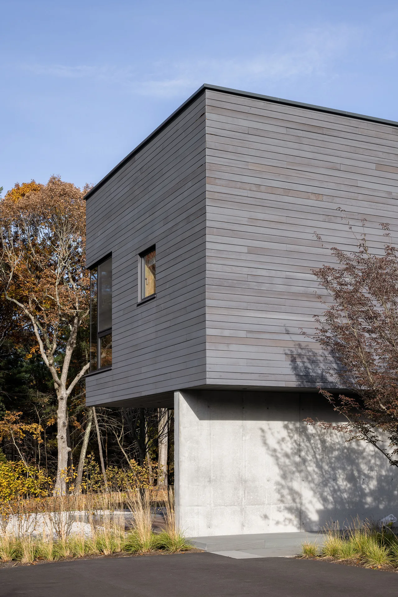 Modern home feature showing dark horizontal wood siding above a concrete foundation with surrounding landscape.