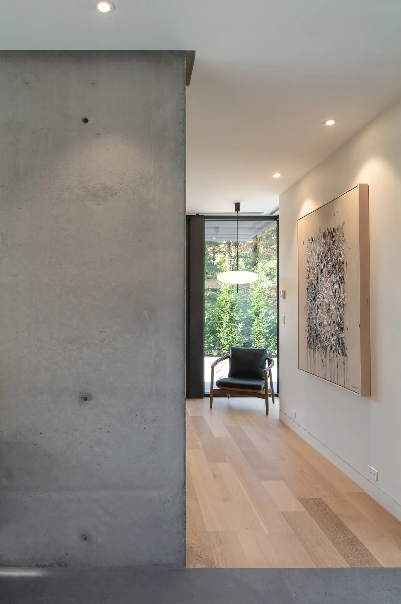 Hallway featuring a textured concrete wall, light wood flooring, a wood frame chair, a pendant light, and a large abstract painting.