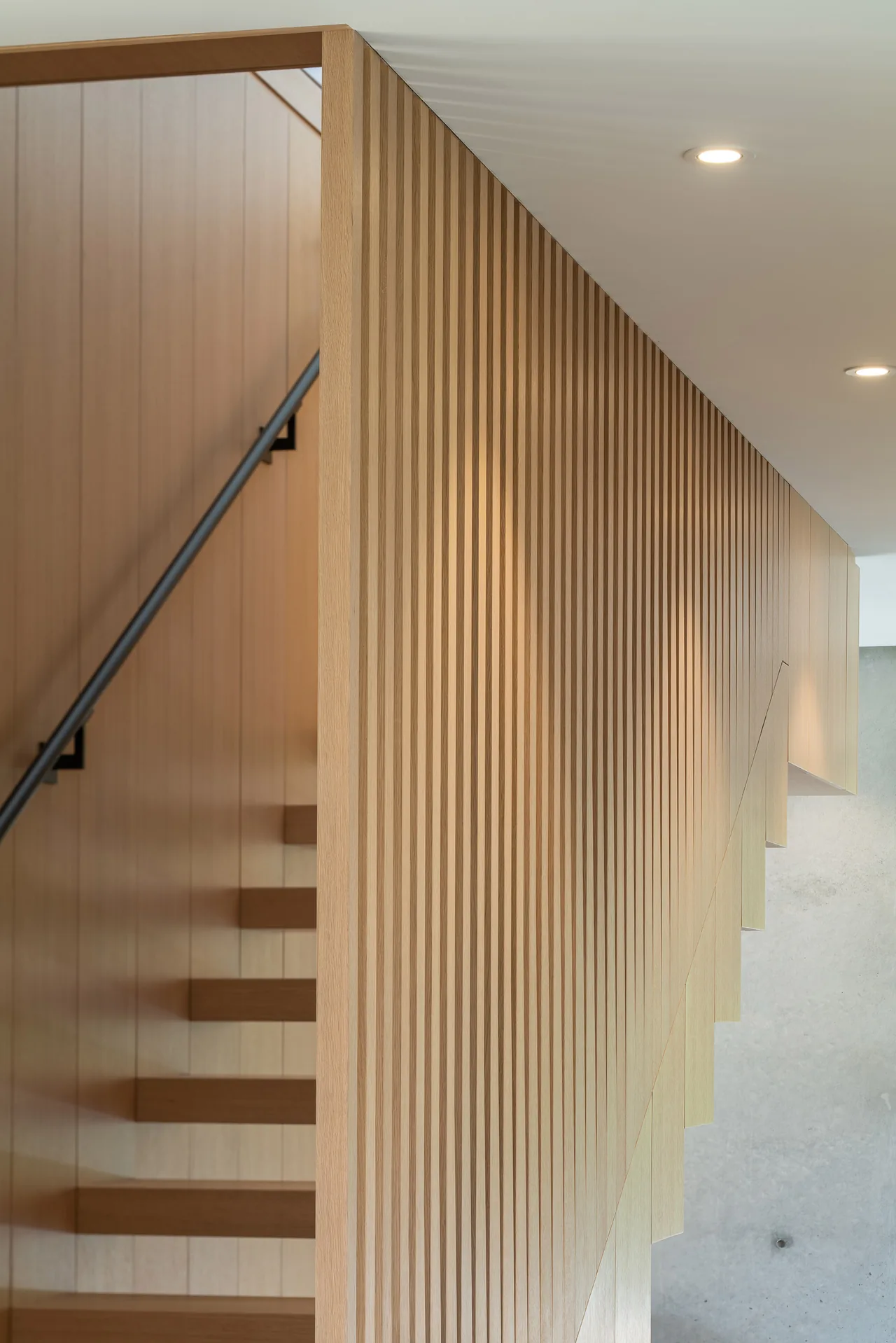 Minimalist interior staircase features vertical wooden slats and floating wooden steps.