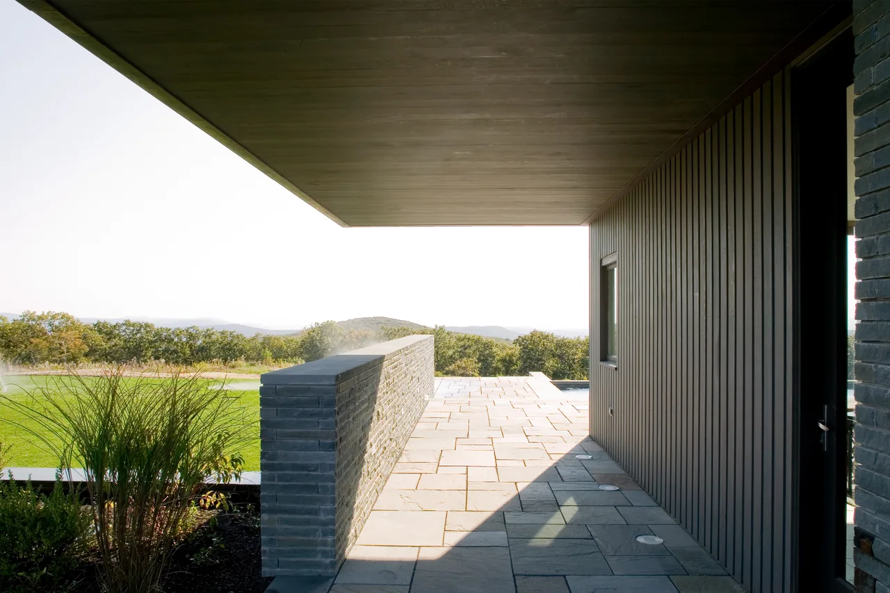 Covered patio with stone tile flooring, vertical siding, and an overhanging flat roof opening to a landscape view.