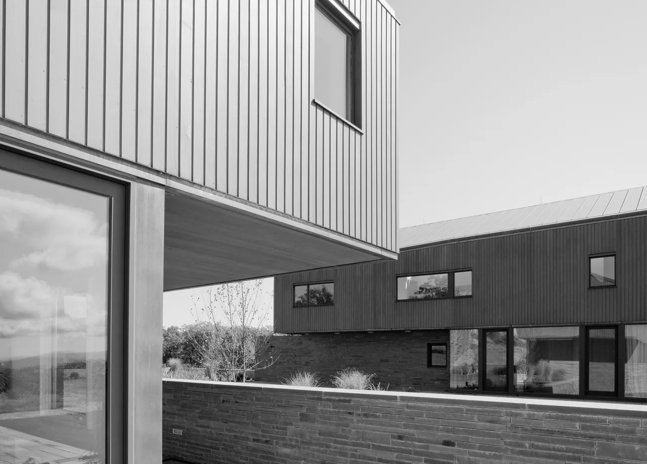 Blue Rock House shows two modern volumes with vertical siding, rectangular windows, a stone retaining wall, and metal roofing.