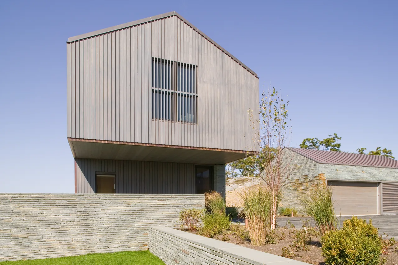 Exterior view of Blue Rock House featuring wood siding, stone walls, and horizontal windows on a two-story structure.