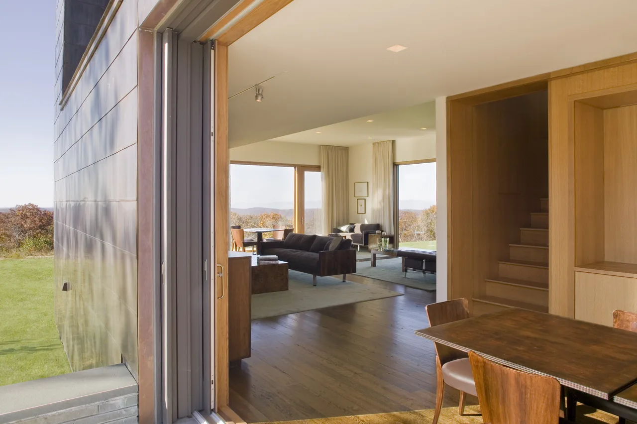 Interior view from dining room to living space featuring floor-to-ceiling windows and wooden finishes.