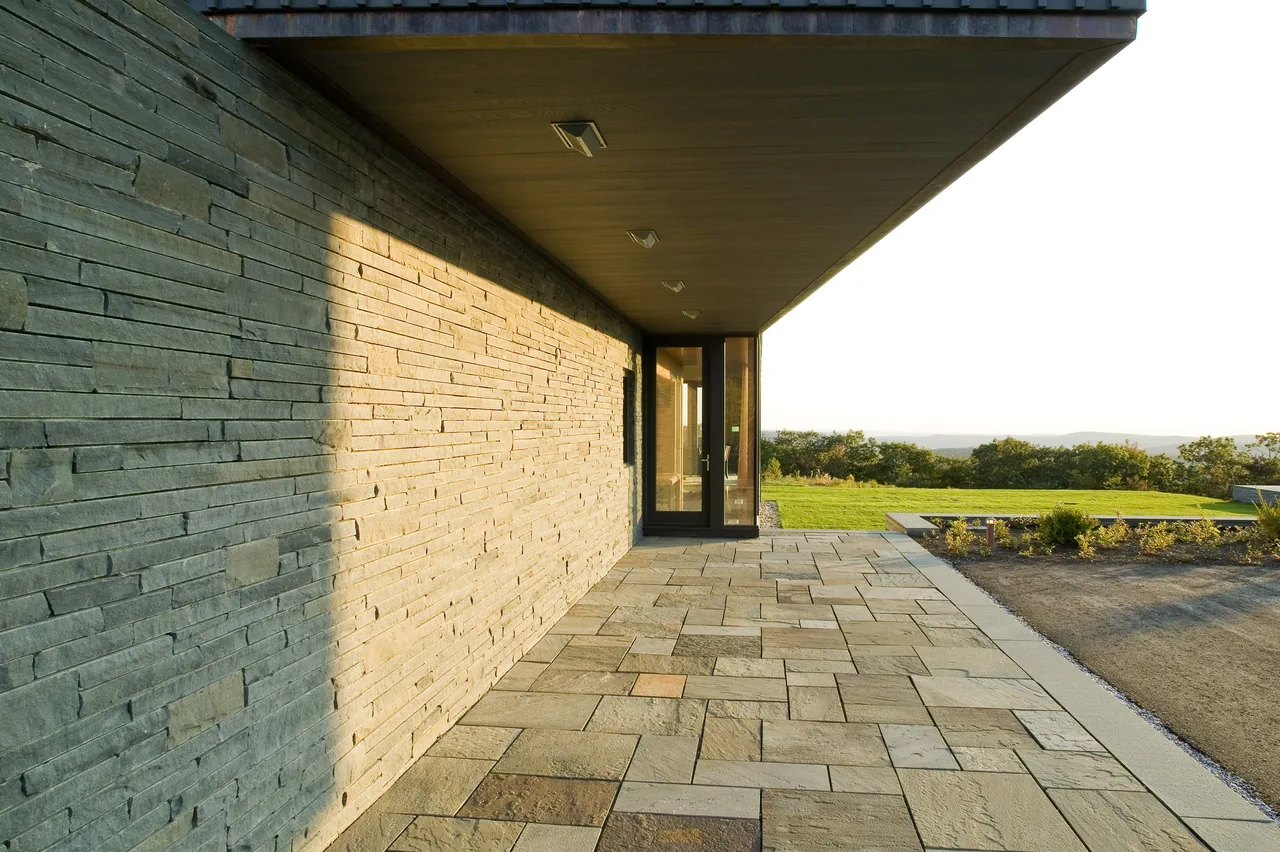 Blue Rock House features a stone wall exterior and a paved courtyard with an overhanging roof.